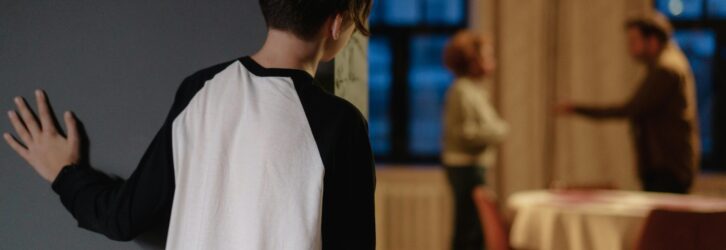 A child watches parents arguing from a doorway in a cozy home setting.